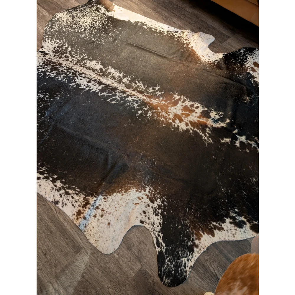 A beautiful extra large cowhide rug in salt and pepper brown with natural speckles laid on a wooden floor
