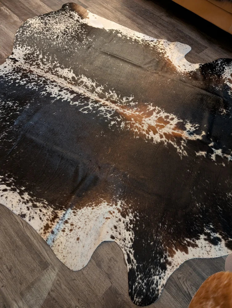 A beautiful extra large cowhide rug in salt and pepper brown with a spotted pattern on a wooden floor