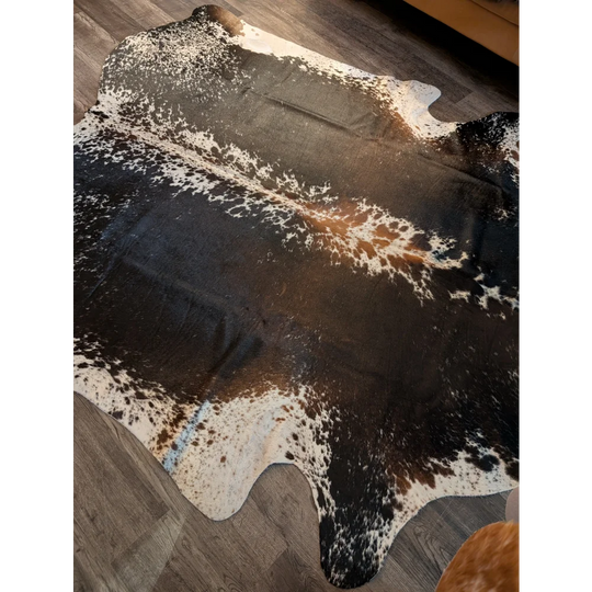 A beautiful extra large cowhide rug in salt and pepper brown with a spotted pattern on a wooden floor