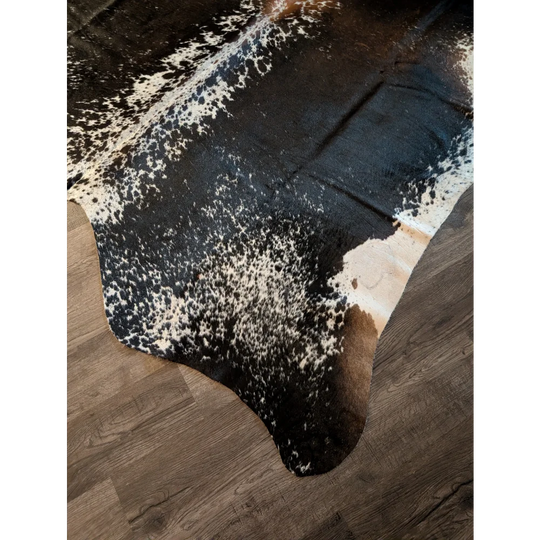 Salt and pepper brown extra large cowhide rug with natural fur texture and black and white spots on wooden floor