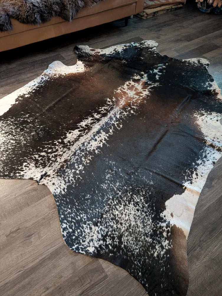 A beautiful extra large salt and pepper brown cowhide rug with a speckled black and white pattern on wooden floor