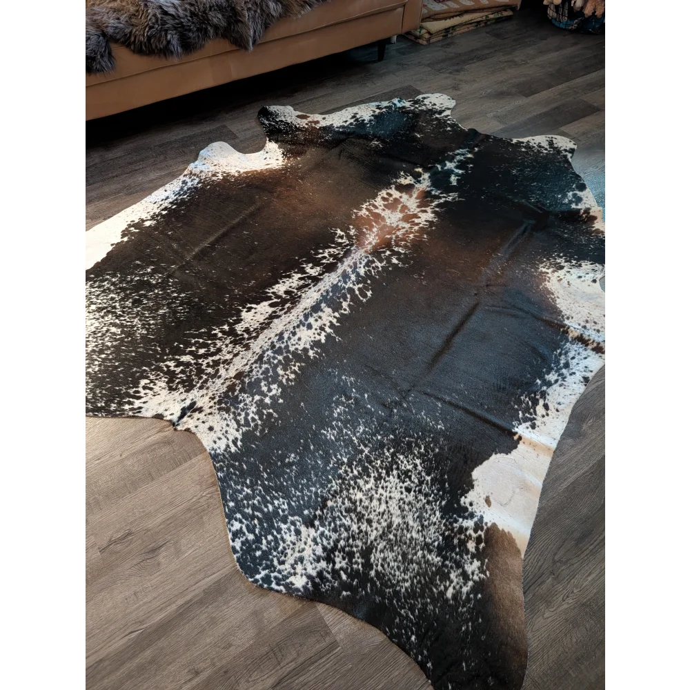 A beautiful extra large salt and pepper brown cowhide rug with a speckled black and white pattern on wooden floor