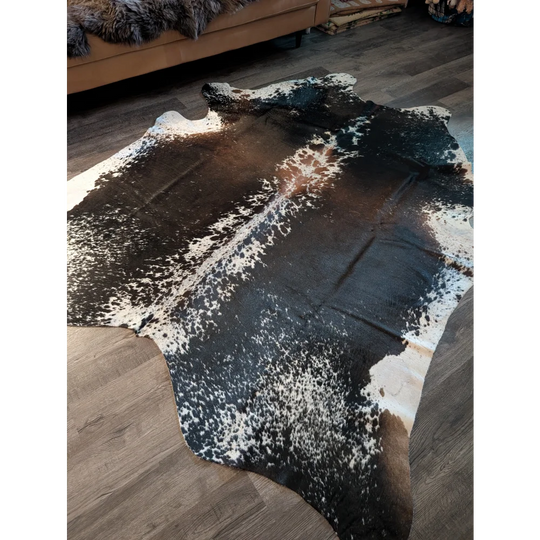 A beautiful extra large salt and pepper brown cowhide rug with a speckled black and white pattern on wooden floor