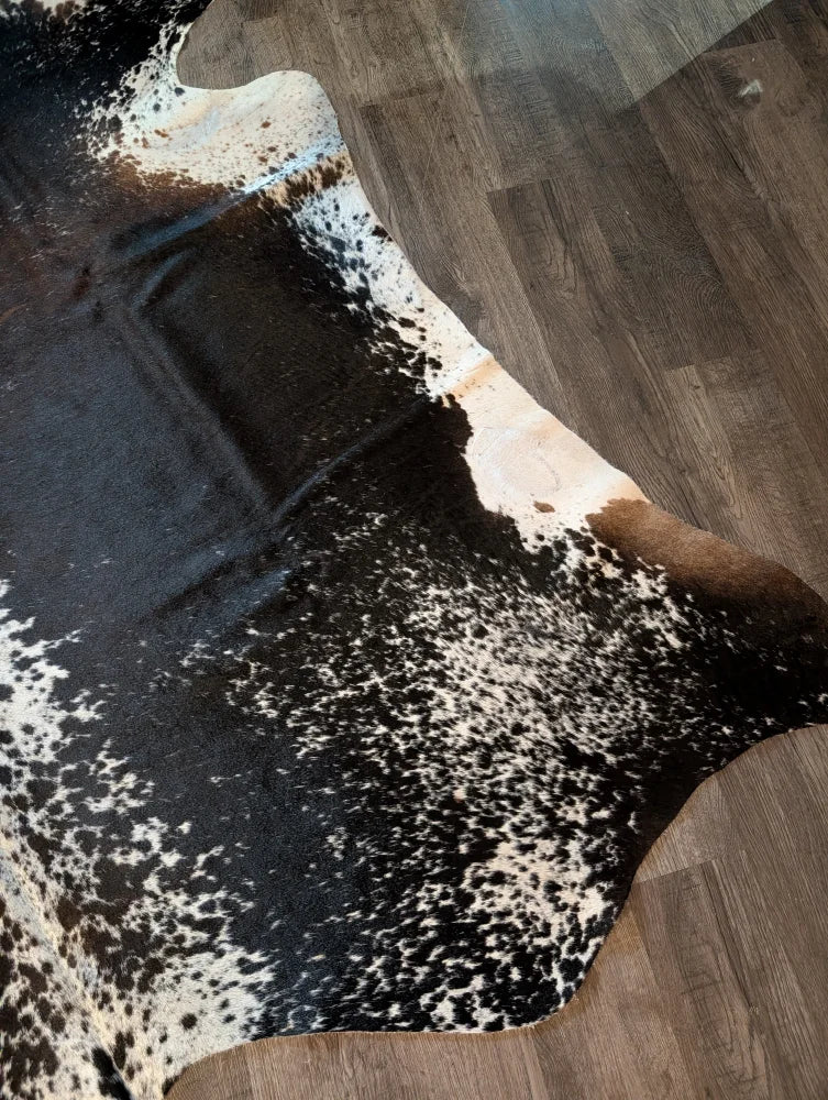 A beautiful extra large black and white speckled cowhide rug salt and pepper brown 91 x 76 on wooden floor