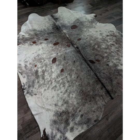Extra large natural white and brown spotted cowhide rug laid flat on dark wood floor perfect large cowhide option