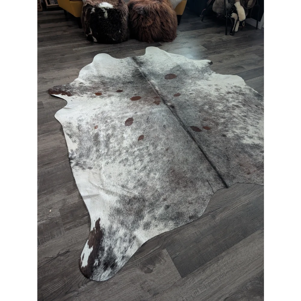 A large extra large cowhide rug saltpepbrn#141 in white and brown with natural markings on dark wood floor