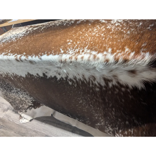 Brown and white speckled faux fur pillow on extra large cowhide rug