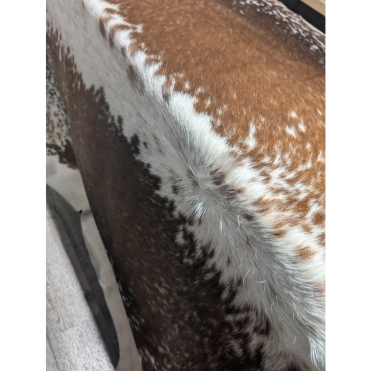 Fluffy brown white speckled faux fur pillow on extra large cowhide rug