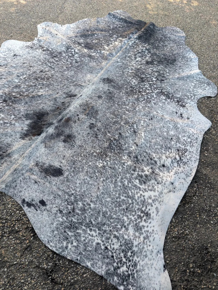 Large speckled gray and black cowhide rug with natural edges showcasing unique characteristics and rustic charm