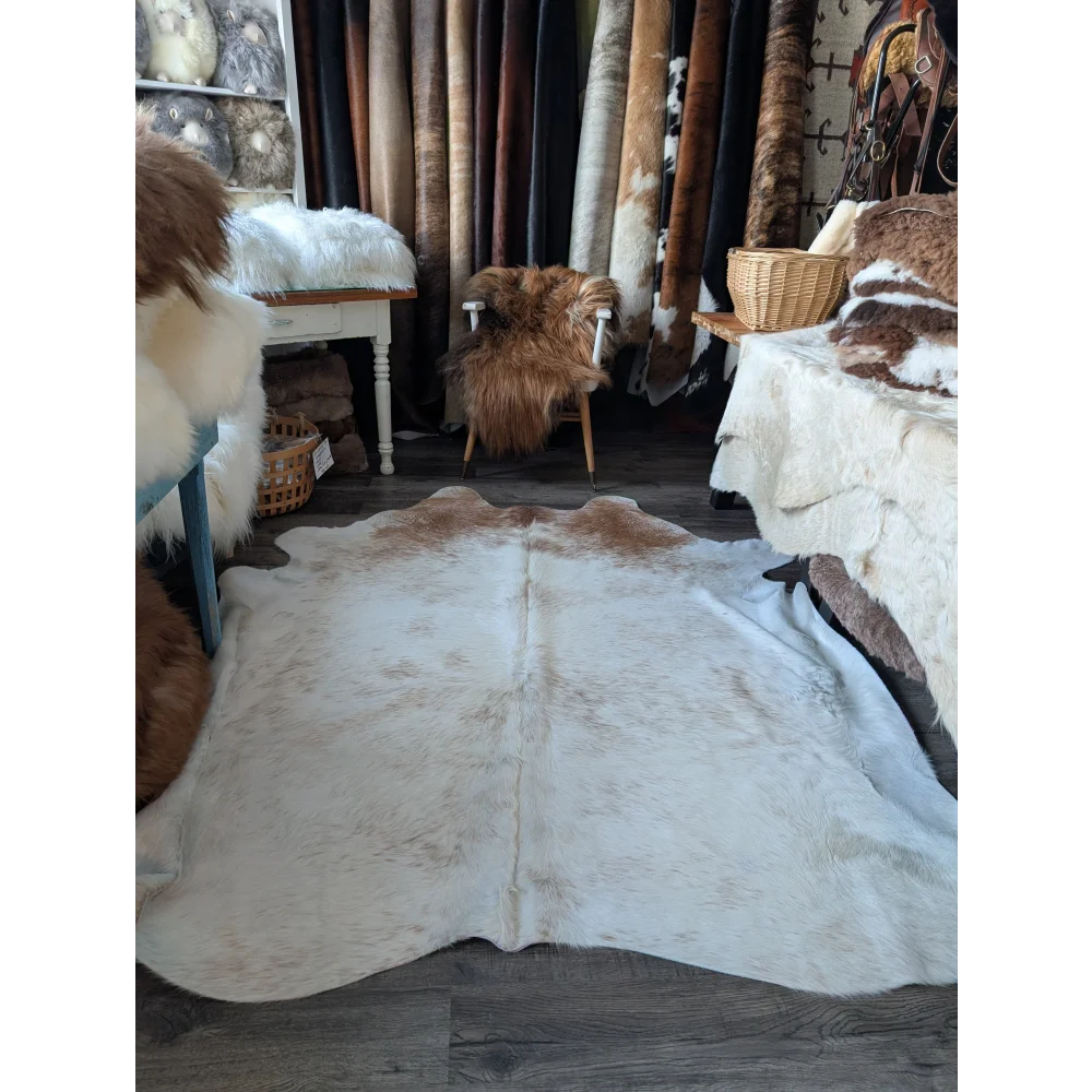 A large cowhide rug by angus oliver featuring a soft fluffy texture in natural white and brown colors