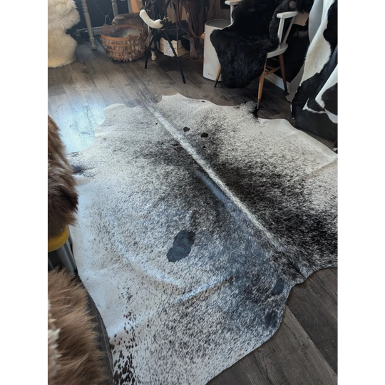 A large cowhide rug salty3 with a white base black speckles and irregular edge adds rustic charm to any room