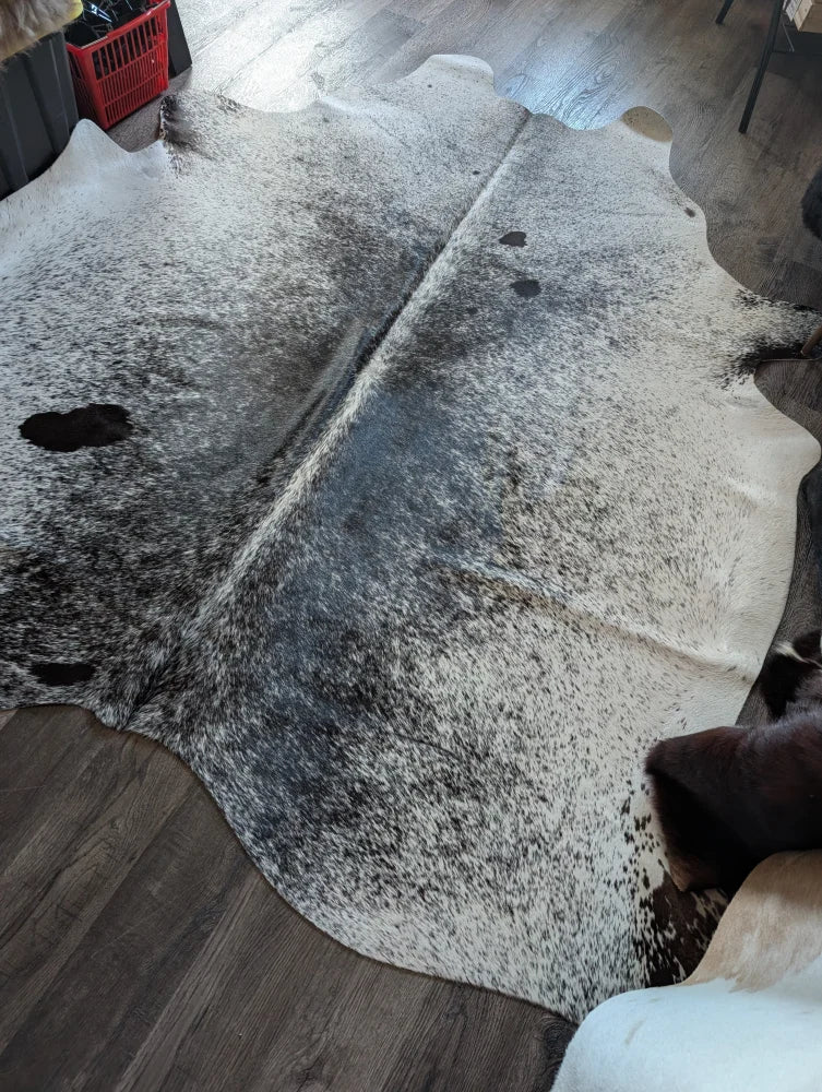 A large cowhide rug with rustic charm featuring a white base and black speckles perfect for beautiful rugs fans