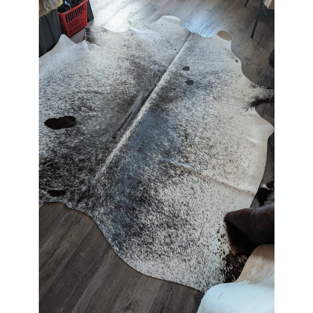 A large cowhide rug with rustic charm featuring a white base and black speckles perfect for beautiful rugs fans
