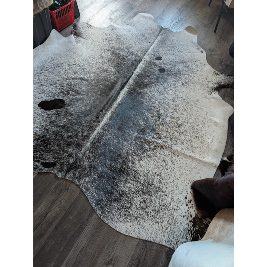 A large cowhide rug with rustic charm featuring a white base and black speckles perfect for beautiful rugs fans