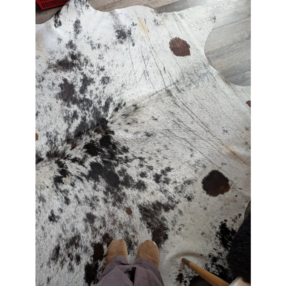 A large cowhide rug salty9 with black and white spots and natural fur texture adding rustic charm to any room