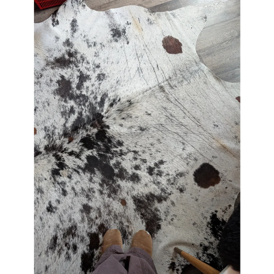 A large cowhide rug salty9 with black and white spots and natural fur texture adding rustic charm to any room