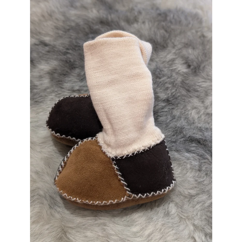 Two-toned brown and black sheepskin baby booties with white stitching and cream cuff