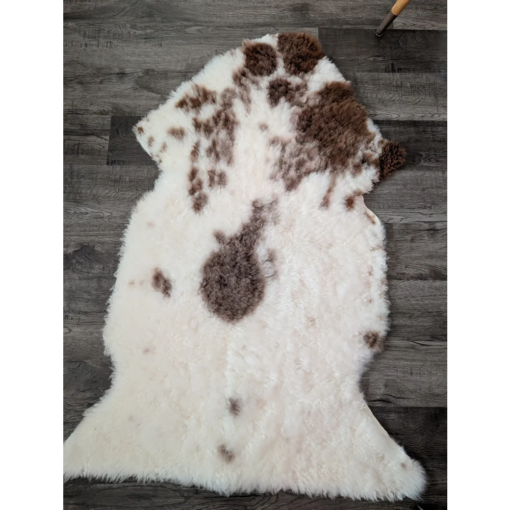 A plush 47.5 x 26 inch tibet highland spotted sheepskin rug with white and brown natural irregular patches
