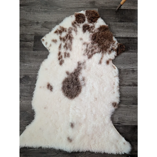 A plush 47.5 x 26 inch tibet highland spotted sheepskin rug with white and brown natural irregular patches
