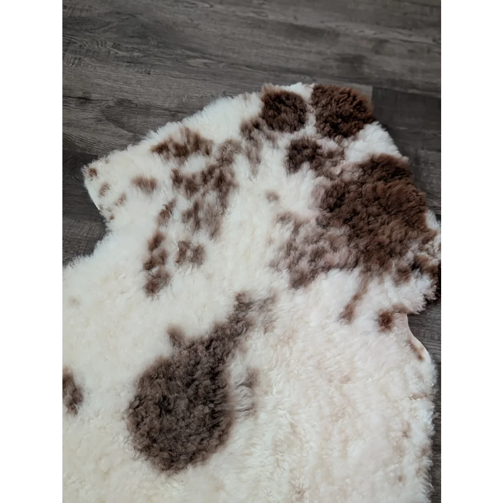 A plush tibet highland spotted sheepskin rug with natural white base and brown patches measuring 47.5 by 26 inches