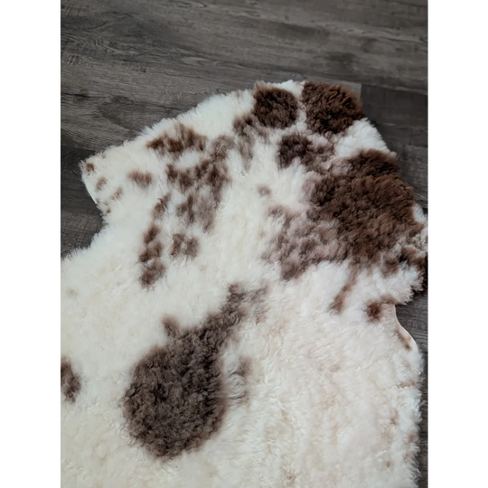 A plush tibet highland spotted sheepskin rug with natural white base and brown patches measuring 47.5 by 26 inches