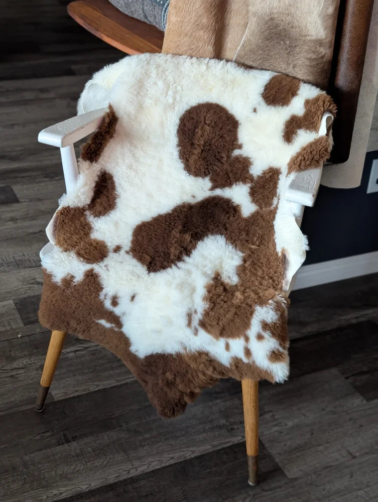 Brown and white tibet highland spotted sheepskin rug draped over wooden chair showing soft texture and natural pattern