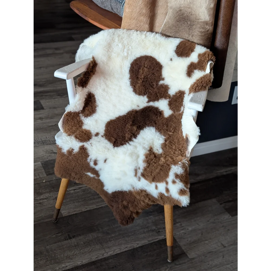 Brown and white tibet highland spotted sheepskin rug draped over wooden chair showing soft texture and natural pattern