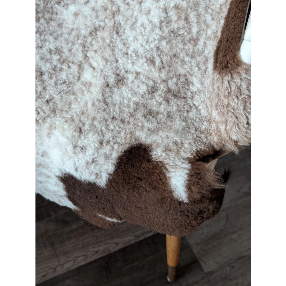 A cozy cream and brown tibet highland spotted sheepskin throw draped over a wooden chair leg