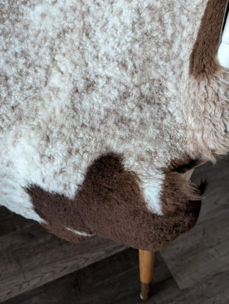 A cozy cream and brown tibet highland spotted sheepskin throw draped over a wooden chair leg