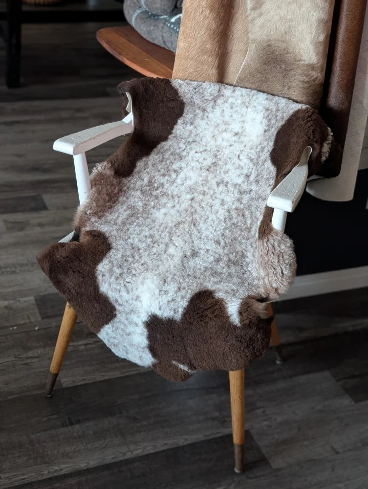A cozy 39 x 26 inch tibet highland spotted sheepskin rug in soft white and brown natural fibers draped over a wooden chair