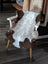 A cozy 39 x 26 inch tibet highland spotted sheepskin rug in soft white and brown natural fibers draped over a wooden chair