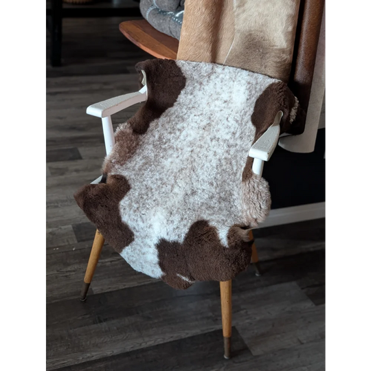 A cozy 39 x 26 inch tibet highland spotted sheepskin rug in soft white and brown natural fibers draped over a wooden chair