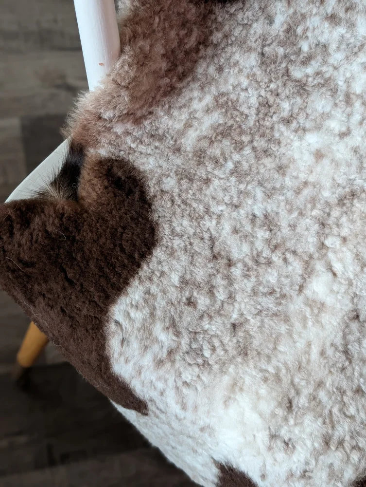 A plush cream and brown tibet highland spotted sheepskin rug with curly texture measuring 39 by 26 inches
