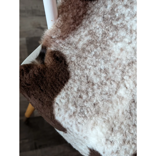 A plush cream and brown tibet highland spotted sheepskin rug with curly texture measuring 39 by 26 inches