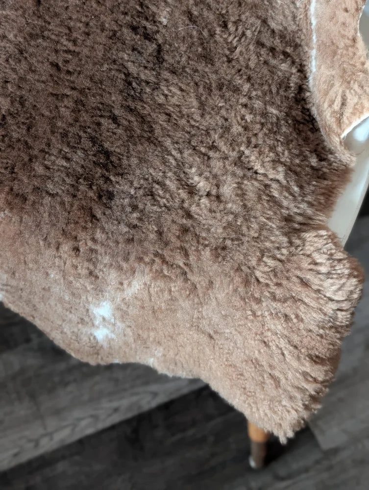 A plush brown tibet highland spotted sheepskin rug with soft shaggy texture and natural white markings, 40 x 25 inches