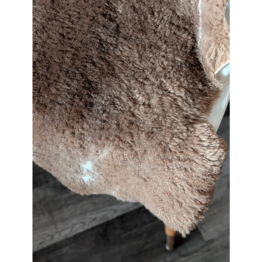 A plush brown tibet highland spotted sheepskin rug with soft shaggy texture and natural white markings, 40 x 25 inches