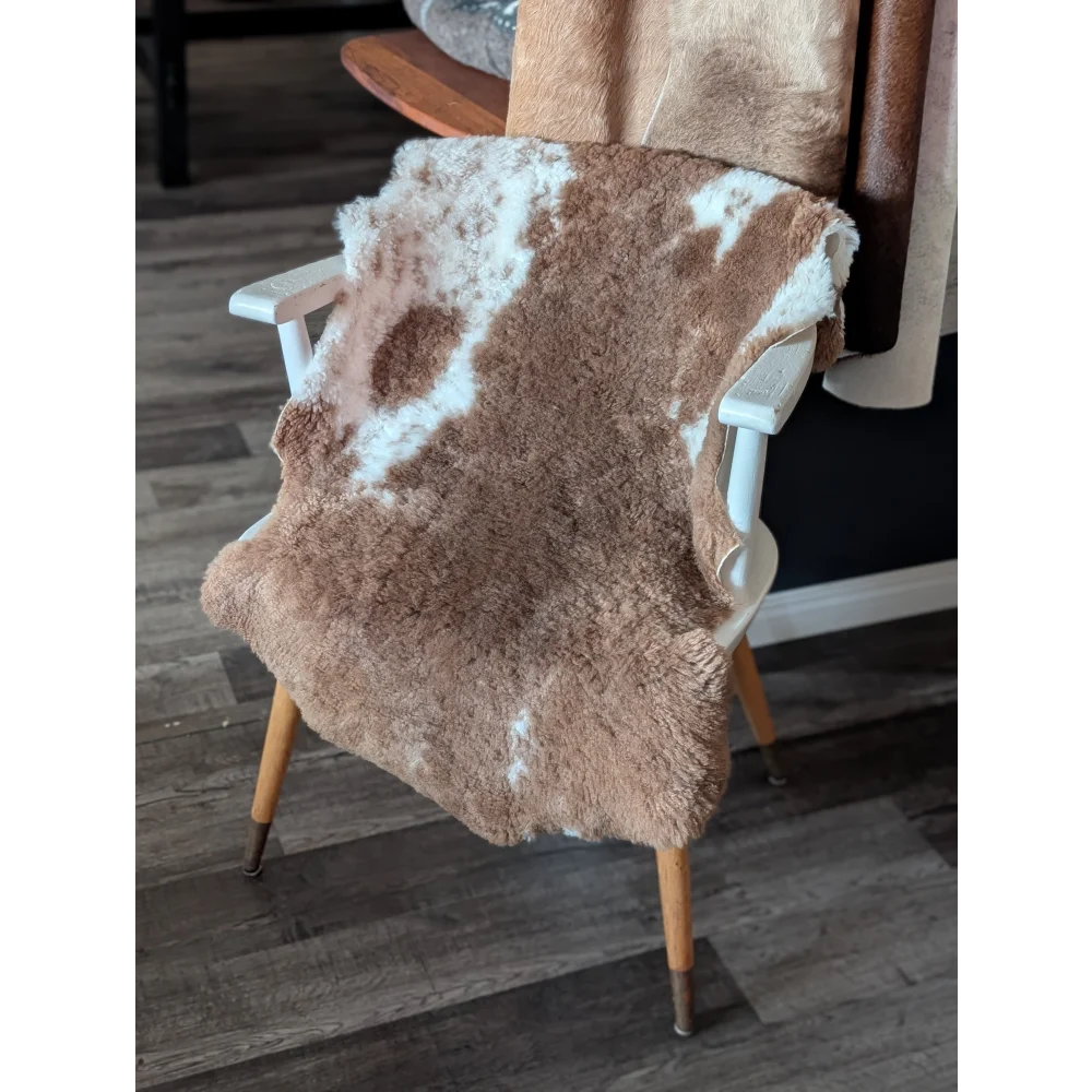 A plush brown and white tibet highland spotted sheepskin rug draped over a white wooden chair with light wood legs