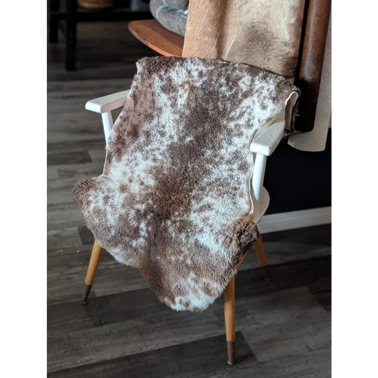 Brown and white speckled tibet highland spotted sheepskin rug draped over wooden chair for cozy decor