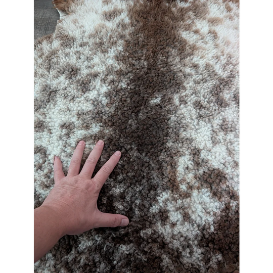 A plush 40x26 inch tibet highland spotted sheepskin rug with curly cream and brown mottled fur grade a quality