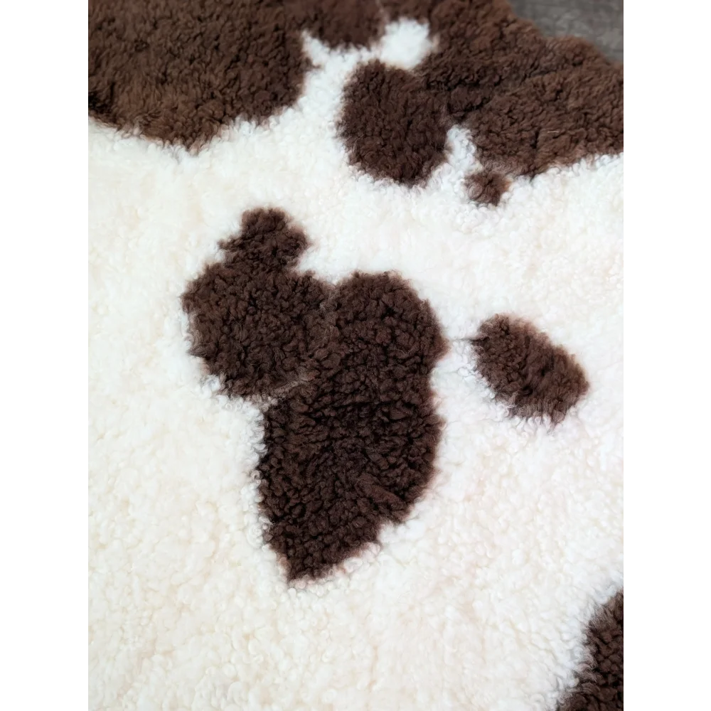 A plush cream-colored tibet highland spotted sheepskin blanket with soft fluffy texture and brown paw print patterns