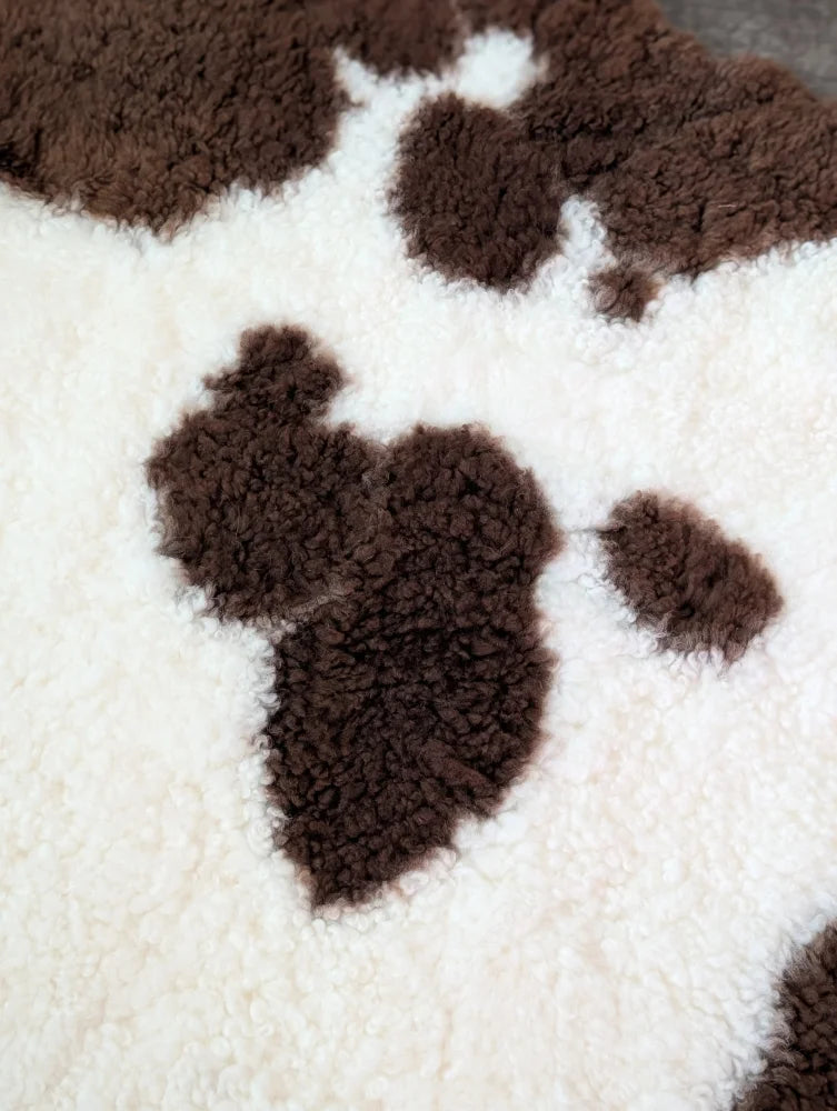 A plush cream-colored tibet highland spotted sheepskin blanket with soft fluffy texture and brown paw print patterns