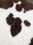 A plush cream-colored tibet highland spotted sheepskin blanket with soft fluffy texture and brown paw print patterns
