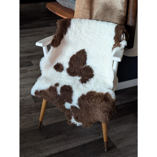 A plush white and brown highland spotted sheepskin throw draped over a wooden chair made from tibet highland spotted material