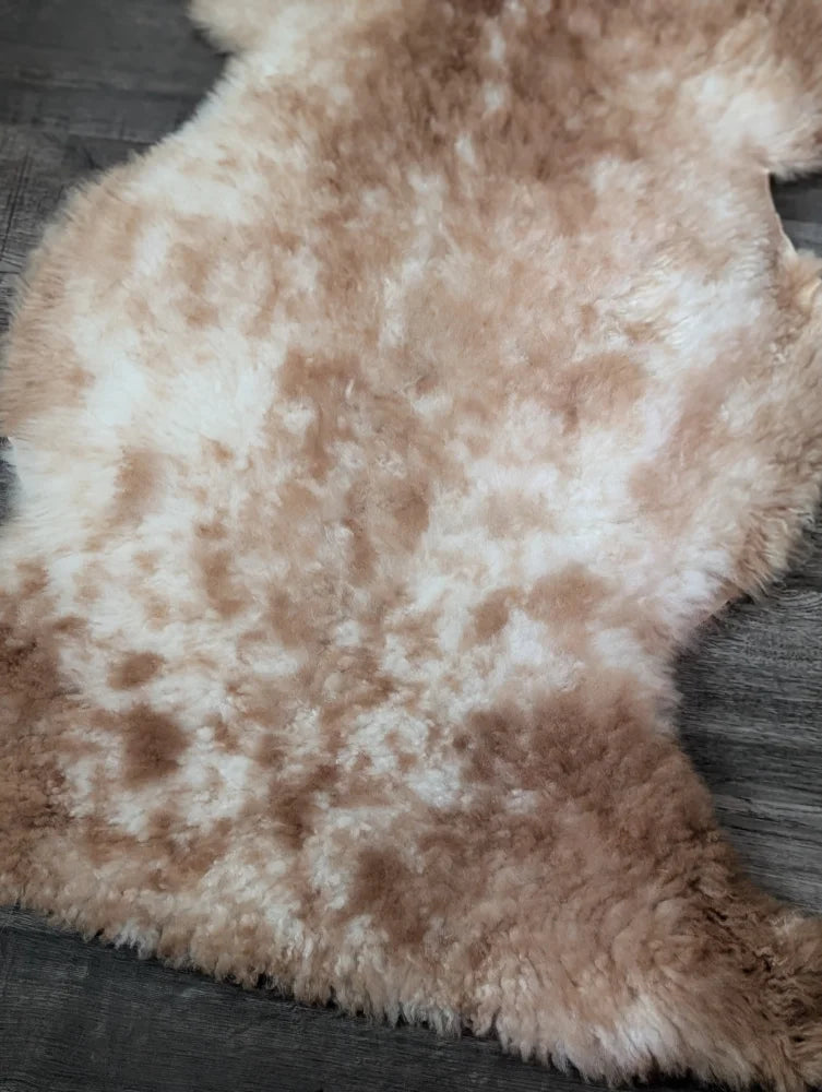 A soft 41.5 x 24.5 inch tibet highland spotted sheepskin rug in creamy white and light brown mottled fur