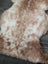 A soft 41.5 x 24.5 inch tibet highland spotted sheepskin rug in creamy white and light brown mottled fur
