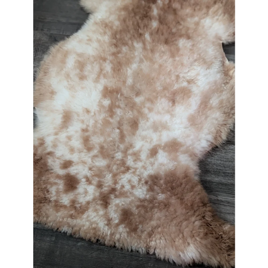 A soft 41.5 x 24.5 inch tibet highland spotted sheepskin rug in creamy white and light brown mottled fur