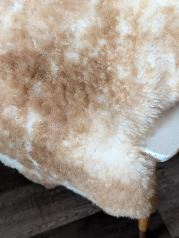 A plush cream and beige tibet highland spotted sheepskin throw with soft fluffy texture measuring 41.5 x 24.5 inches