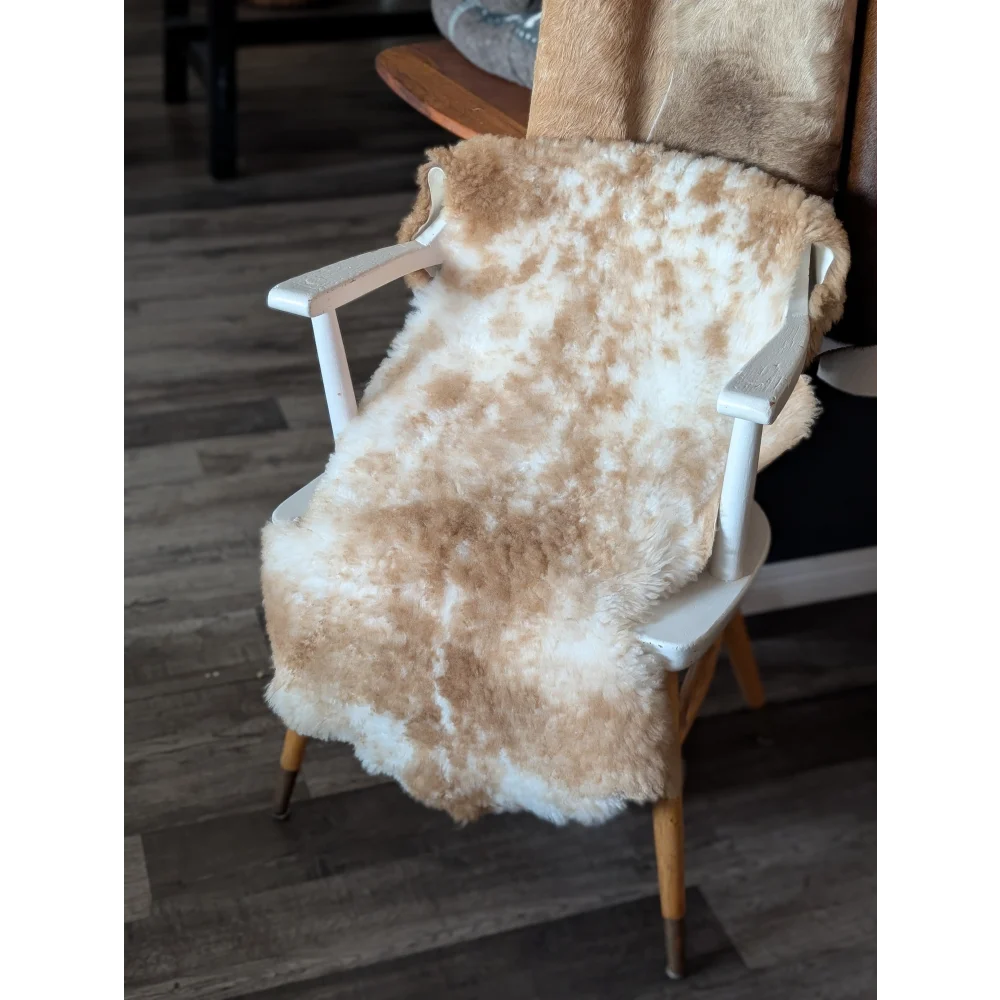 A cozy cream and white highland spotted sheepskin throw draped over a white wooden chair for stylish comfort