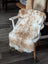 A cozy cream and white highland spotted sheepskin throw draped over a white wooden chair for stylish comfort