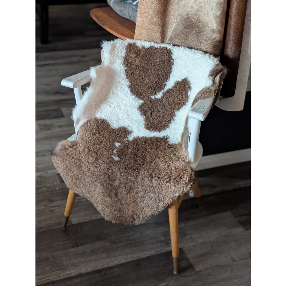 A cozy plush tibet highland spotted sheepskin blanket in natural brown and white draped over a wooden chair